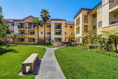 a pathway leading to an apartment building with grass and a bench